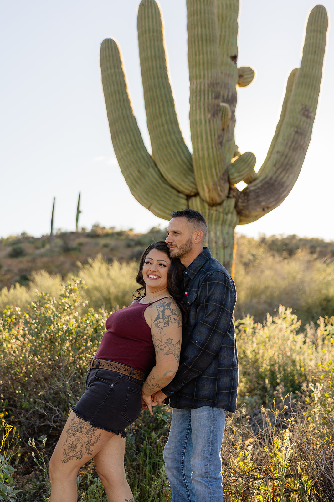 A couple taking engagement photos in front of a cactus