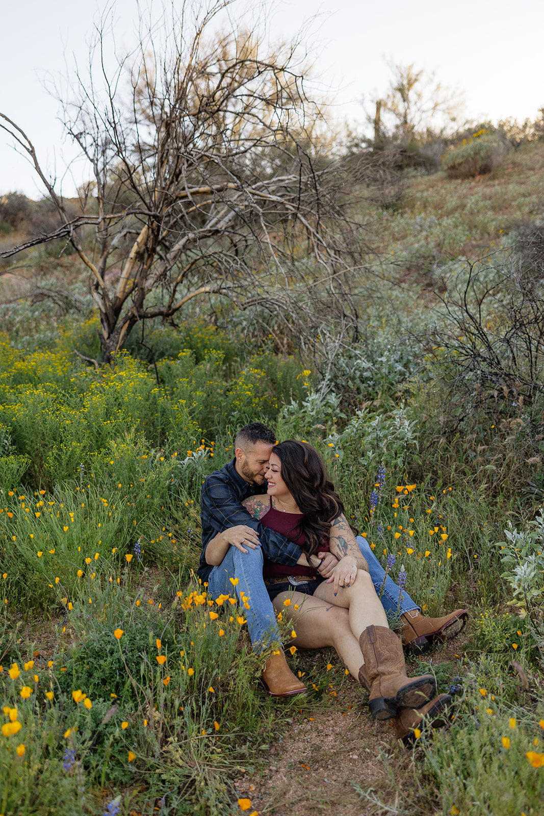 A couple sitting in a field for engagement photos at Bartlett Lake in Arizona
